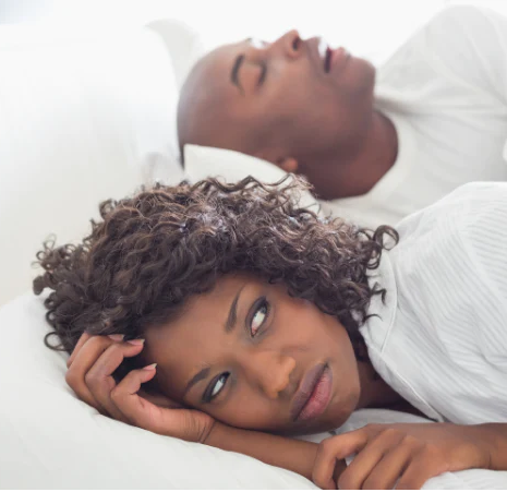 A man snoring and a woman visibly irritated beside him, snoring remedies
