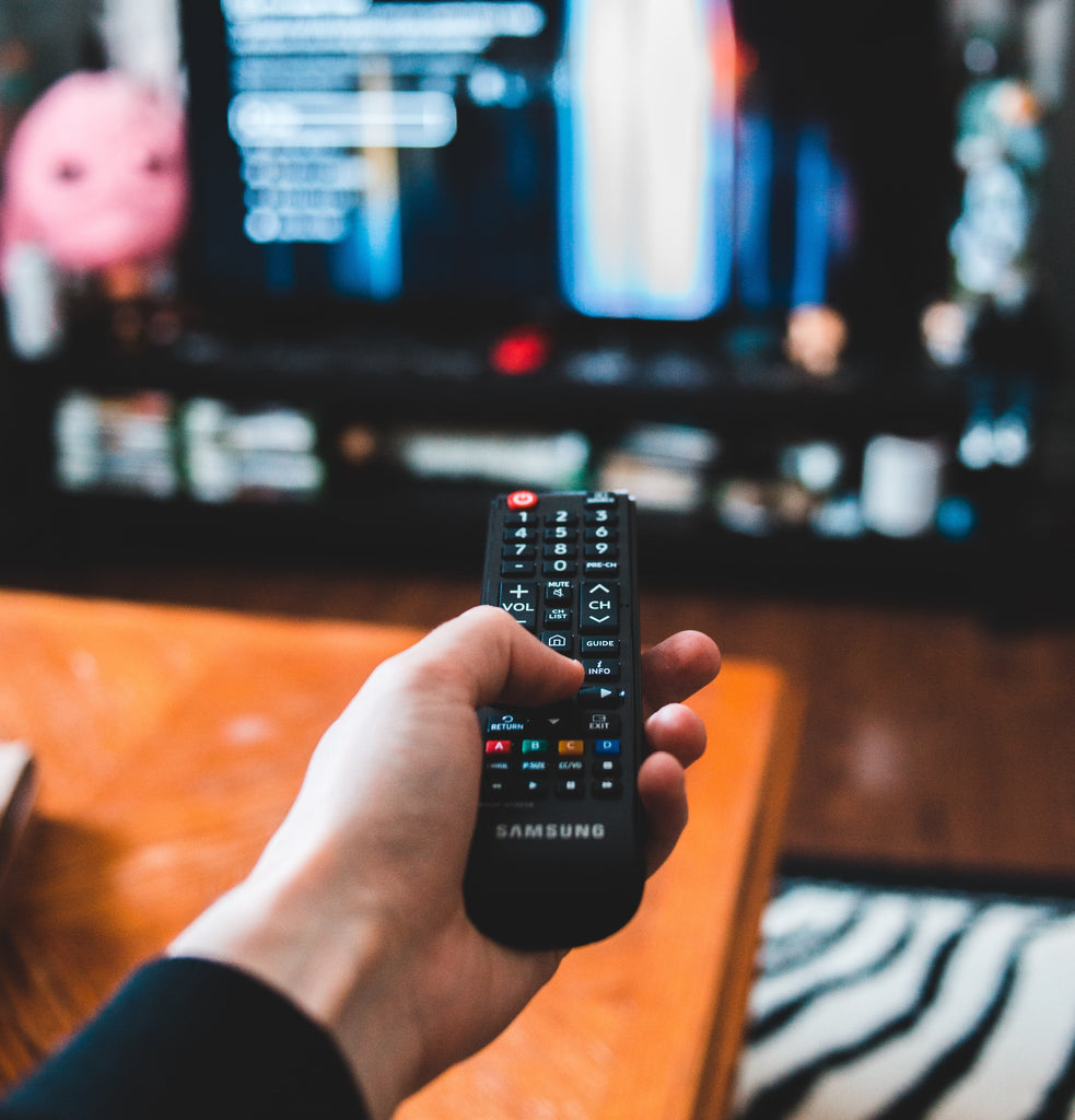 A hand holding a remote control pointed to a TV, blog content is about sleep loss due to binge-watching