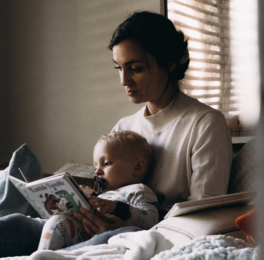Woman with a baby on her lap, reading a book. Understanding the 5 Stages of sleep and the sleep cycle