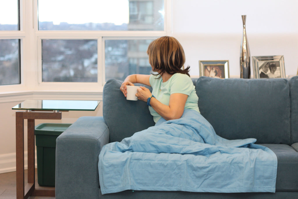 Infrared Health Blanket for Kids Product Image. Woman sitting on couch enjoying a cup of tea with the blanket over her legs.
